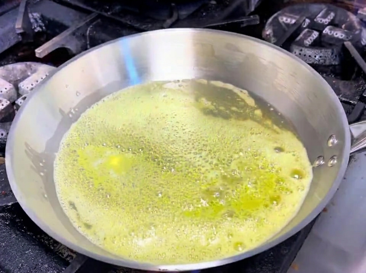 Ajo y chalotas chisporroteando en mantequilla derretida dentro de una sartén de acero inoxidable.