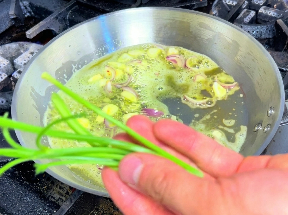 Tallos de perejil siendo salteados junto con ajo y chalotas en una sartén con mantequilla.