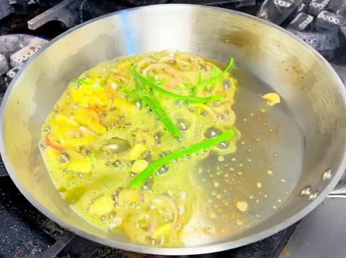 Ajo en láminas, chalotas y chiles verdes chisporroteando en mantequilla derretida en una sartén.