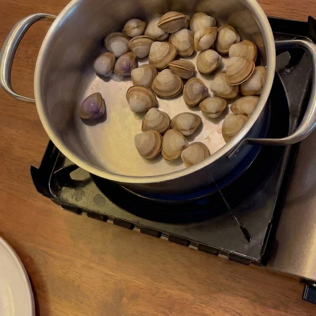 Vino siendo vertido en una olla con almejas, papas y zanahorias, que están sobre una estufa portátil.