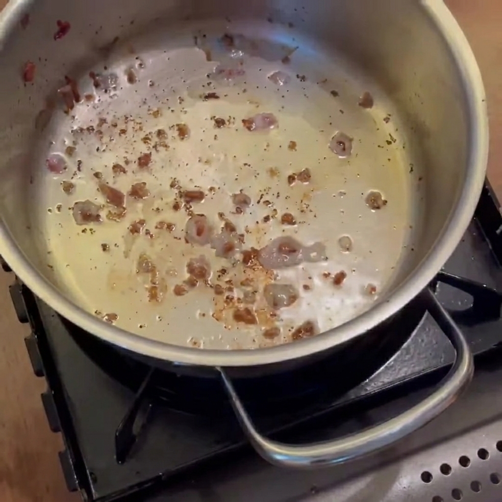 Cebollas, zanahorias y papas sofríéndose en la olla con grasa de tocino hasta quedar translúcidas.