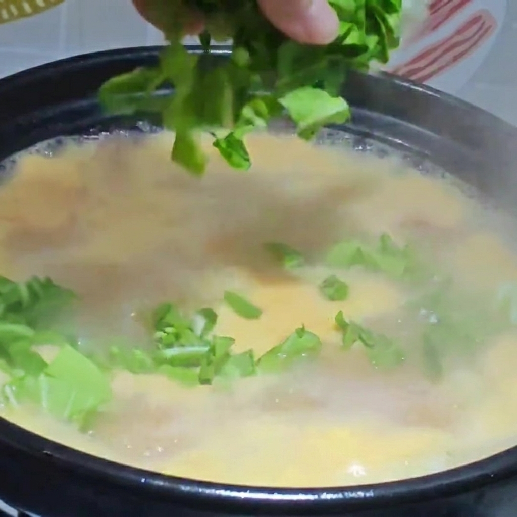 Vegetales picados y pollo deshebrado siendo añadidos a una olla de sopa de masa hirviendo.