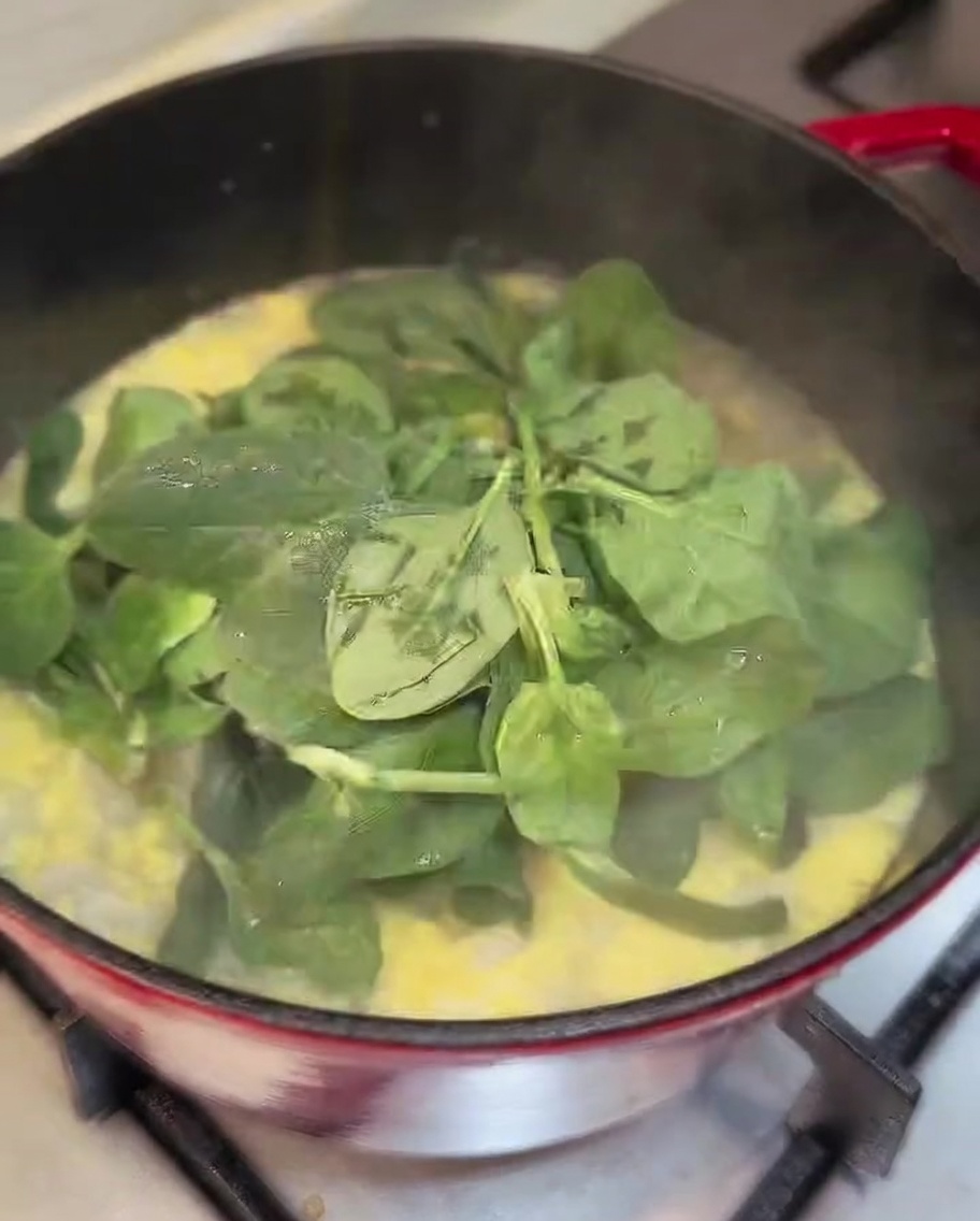 Hojas de espinaca fresca siendo añadidas a una olla de sopa de pollo terminada.