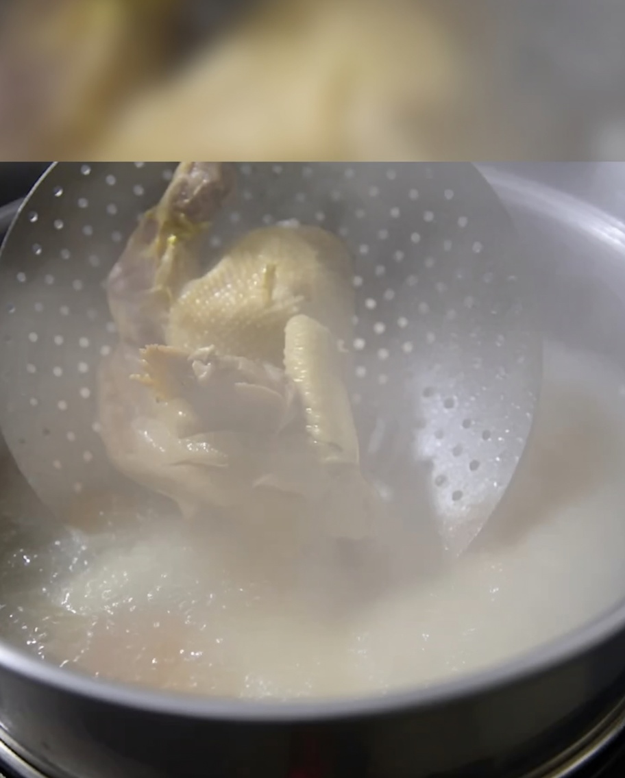 Un pollo entero cocido introduciéndose en una olla de caldo de huesos a fuego lento.
