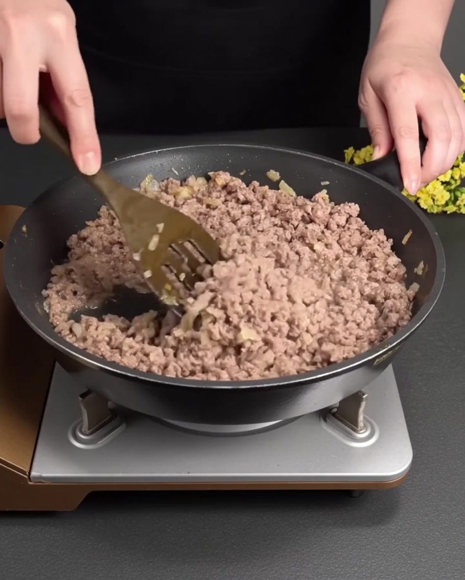 Carne molida dorándose y separándose en una sartén caliente mezclada con los aromáticos ablandados.