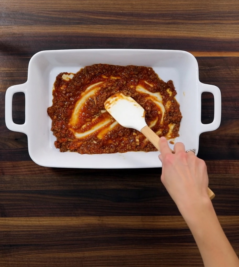Primer plano de una fuente de horno mostrando las distintas capas de salsa de carne, pasta tierna y salsa blanca.