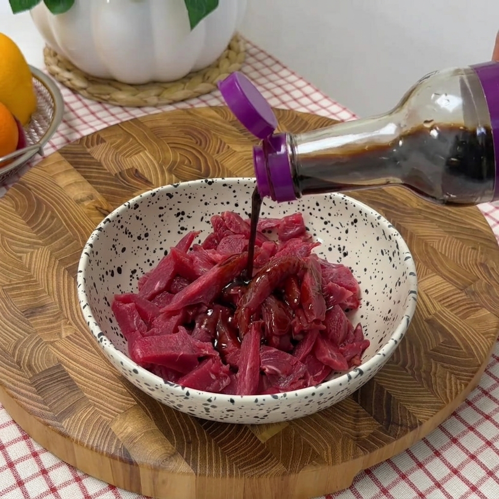 Tiras de ternera en un bol siendo condimentadas con salsas de soja, pimienta negra y aceite.