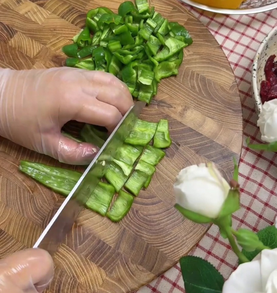 Pimientos y cebolla roja picados en trozos pequeños sobre una tabla de cortar.