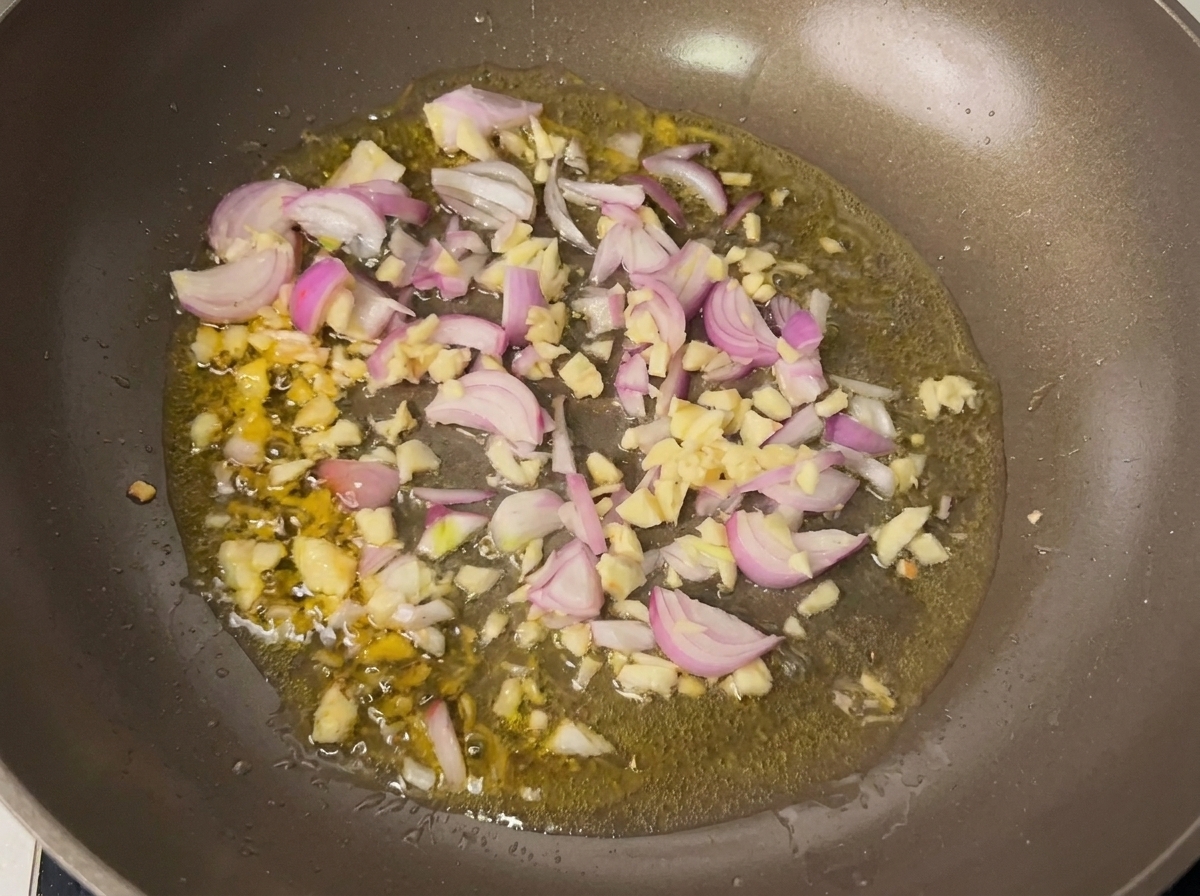 Ajo y chalotas sofriéndose en aceite caliente en una sartén.