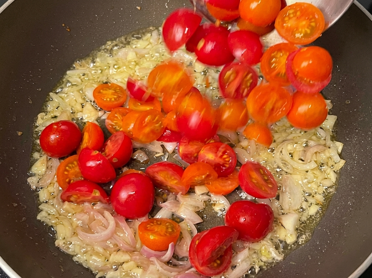 Aromáticos sofritos y tomates cherry cocinándose juntos en una sartén.