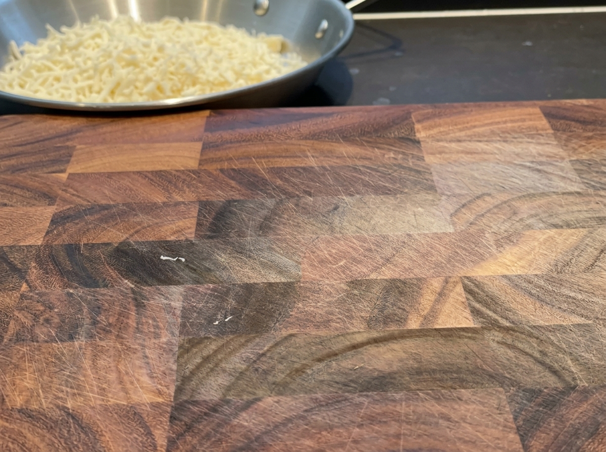 Láminas de queso cheddar cortándose en tiras uniformes sobre una tabla de madera.