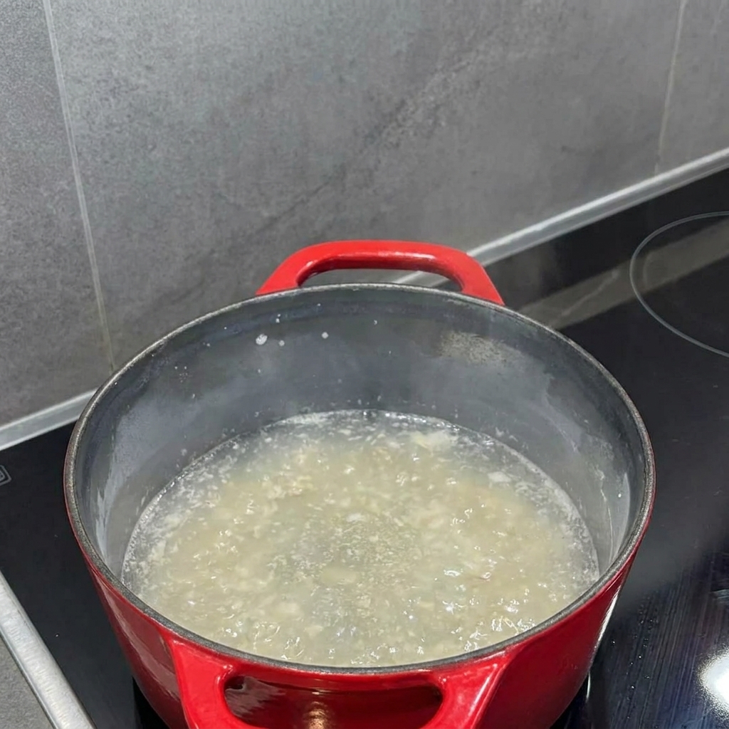 Leche vertiéndose en el roux dentro de una olla, mientras un batidor la integra en un líquido suave.