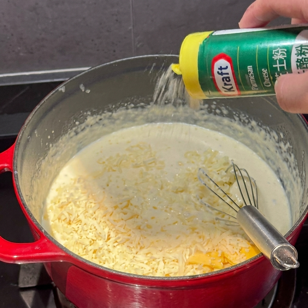 Queso en polvo espolvoreándose desde un recipiente en una olla de salsa de queso cremosa.