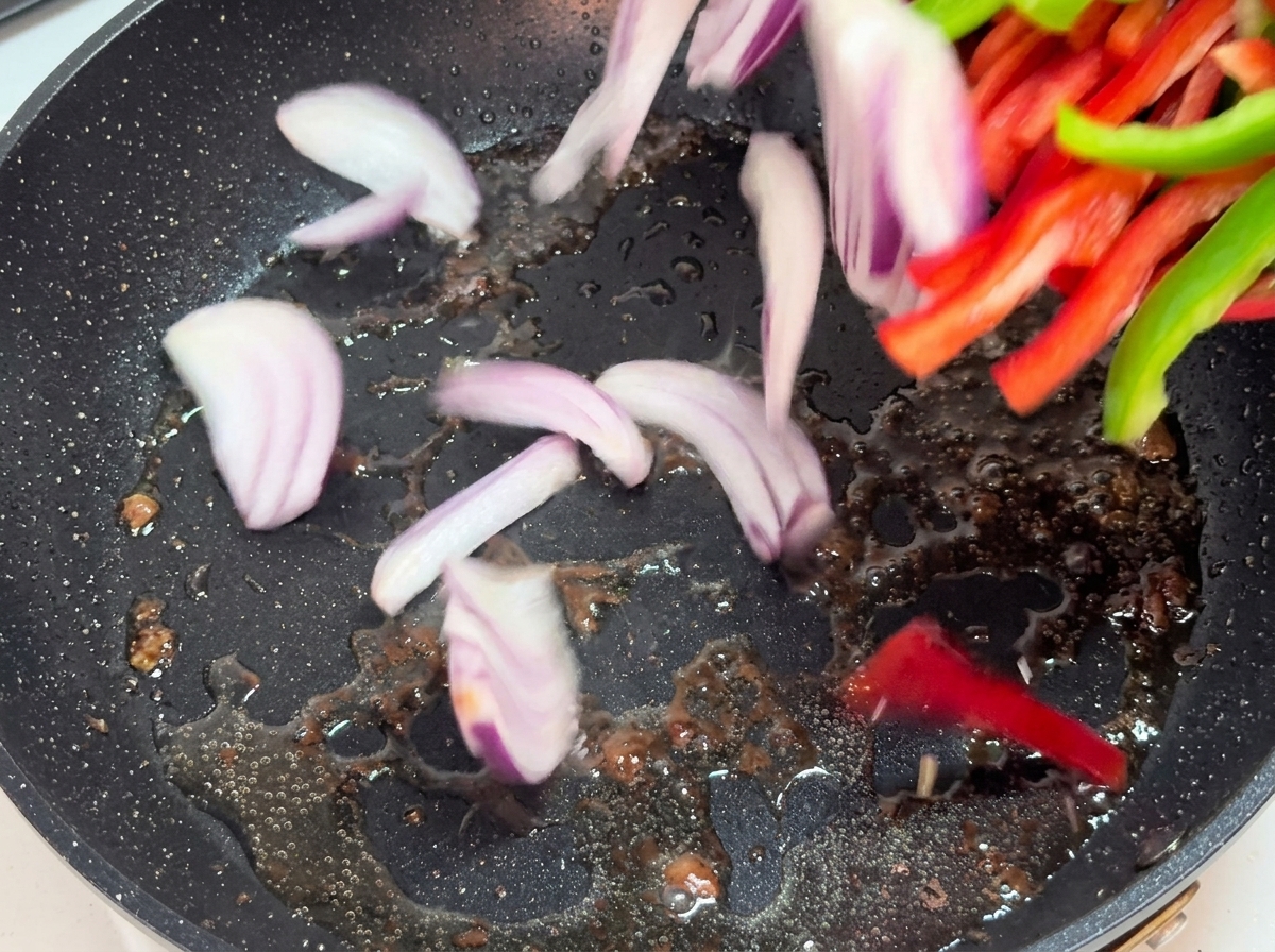 Tiras de cebolla y pimiento salteándose en una sartén caliente.