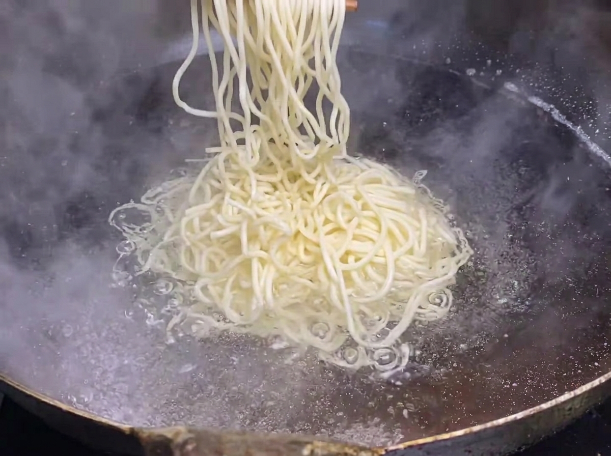 Fideos frescos siendo sumergidos en una olla grande con agua hirviendo.