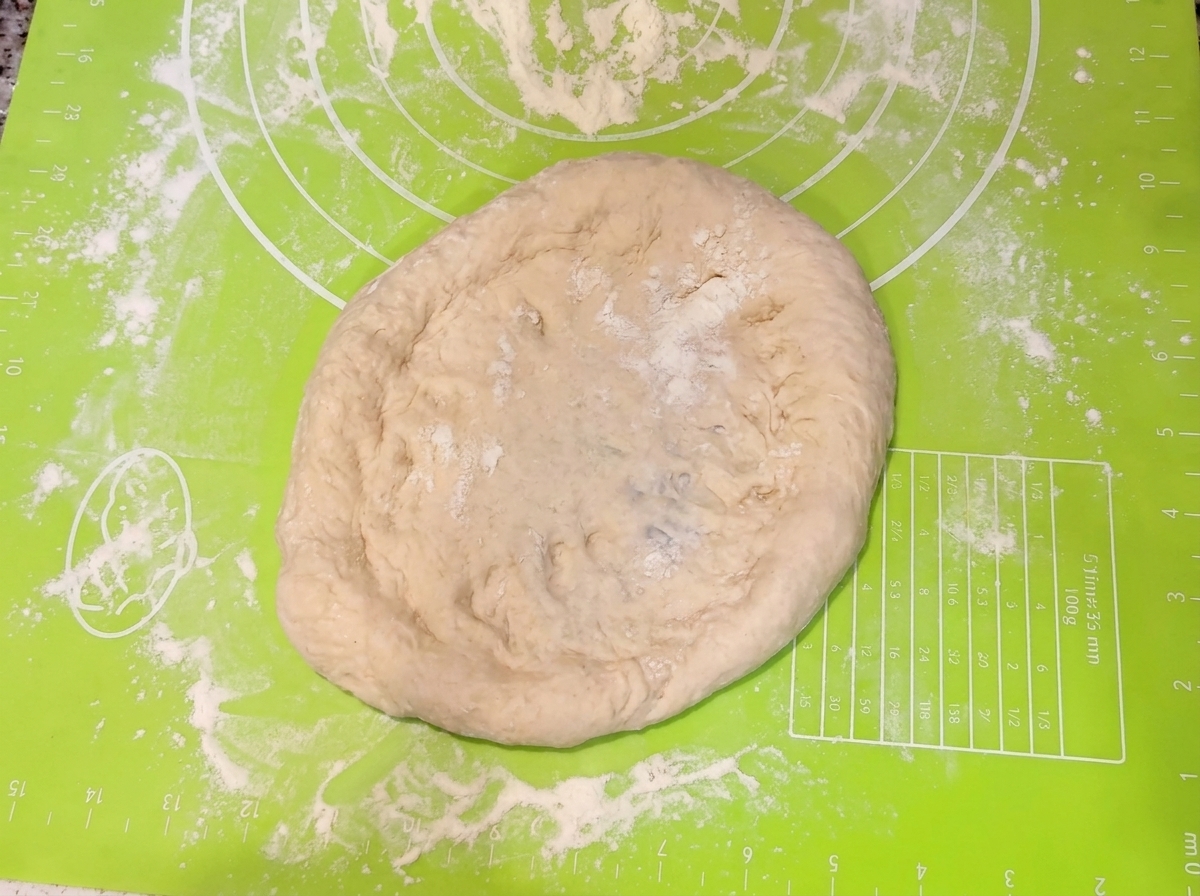 Manos presionando y dando forma a la masa de pizza en un círculo sobre una alfombrilla verde.