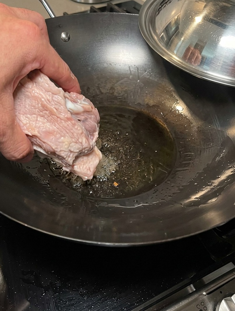 Huesos de cerdo siendo sellados en un wok caliente y seco para desarrollar una base de sabor tostado.