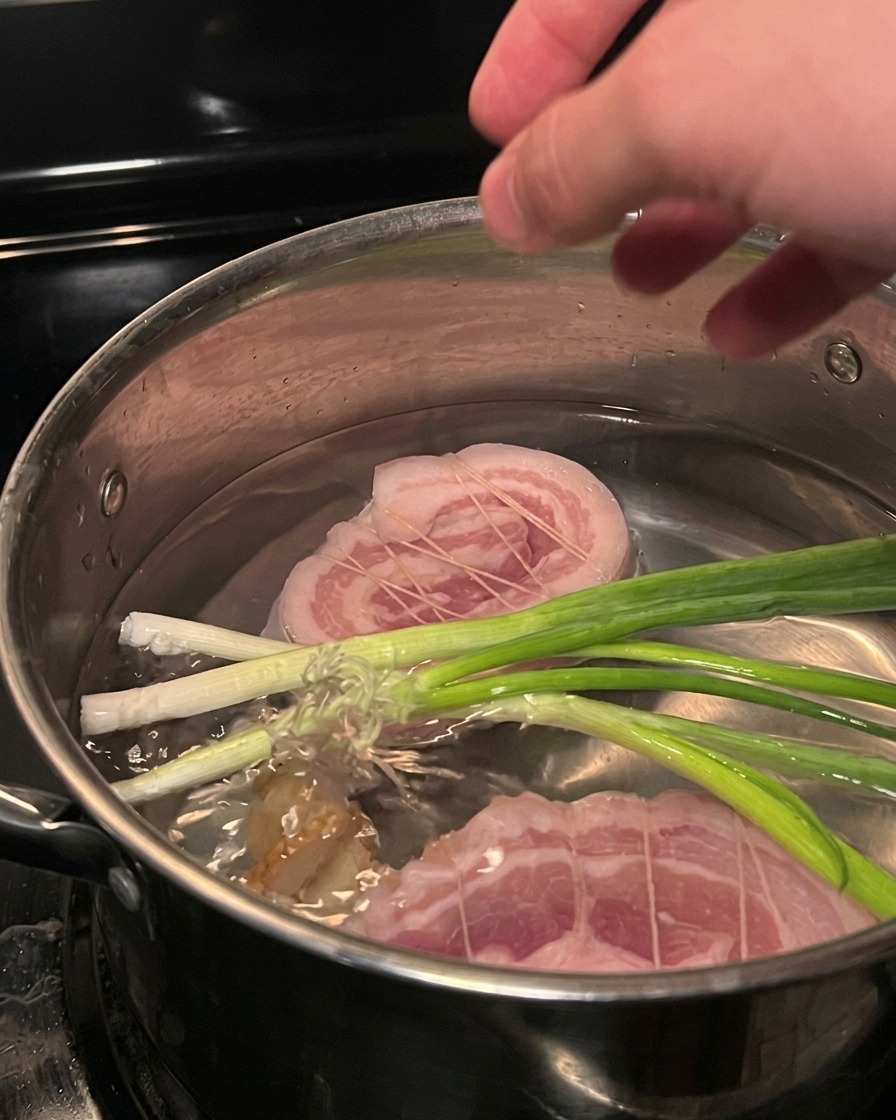 Panceta de cerdo atada hirviendo en una olla con cebolletas.