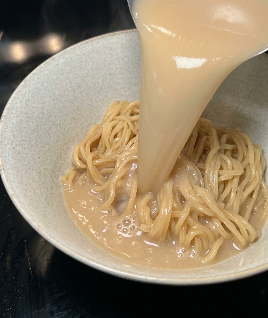 Caldo tonkotsu caliente y cremoso siendo servido en un bol sobre fideos cocidos.