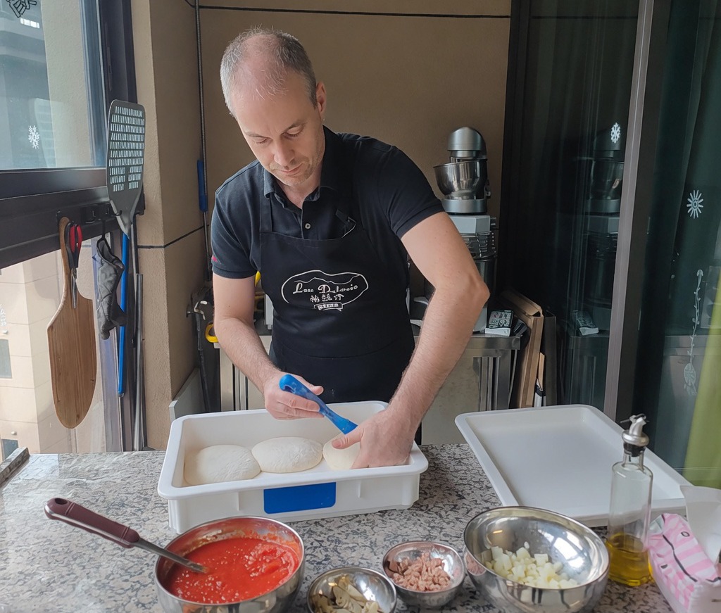 Primer plano de manos presionando una bola de masa fermentada sobre una superficie enharinada para crear la base de la pizza.