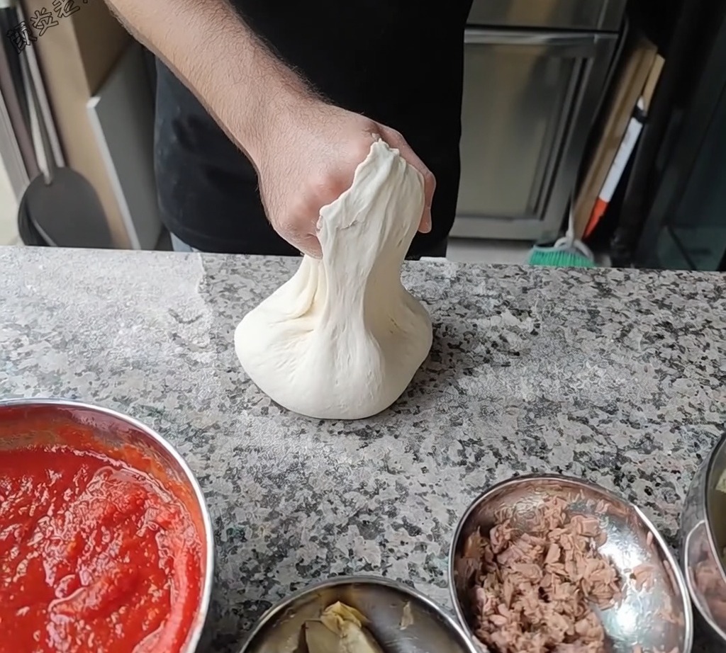 Chef estirando la masa de pizza rotándola sobre sus nudillos para lograr el diámetro deseado.