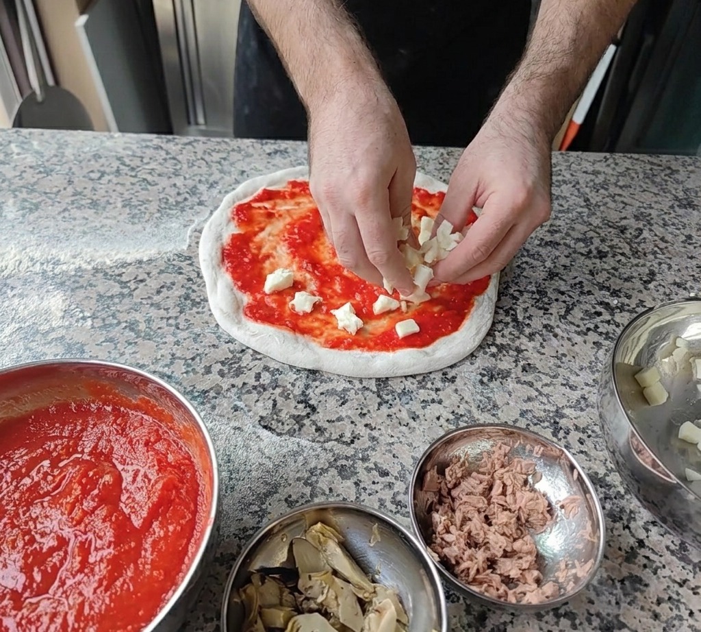 Pequeños cubos de queso mozzarella blanco fresco esparcidos sobre la base de salsa de tomate.