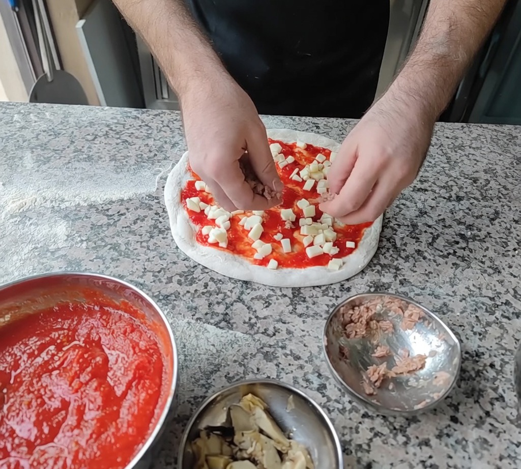 Añadiendo lascas de atún y rodajas de alcachofa a la pizza como ingredientes finales.