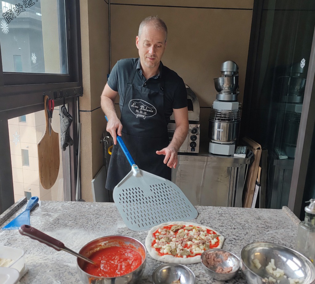 Una pala de metal deslizándose bajo la pizza cruda ensamblada para prepararla para el horneado.