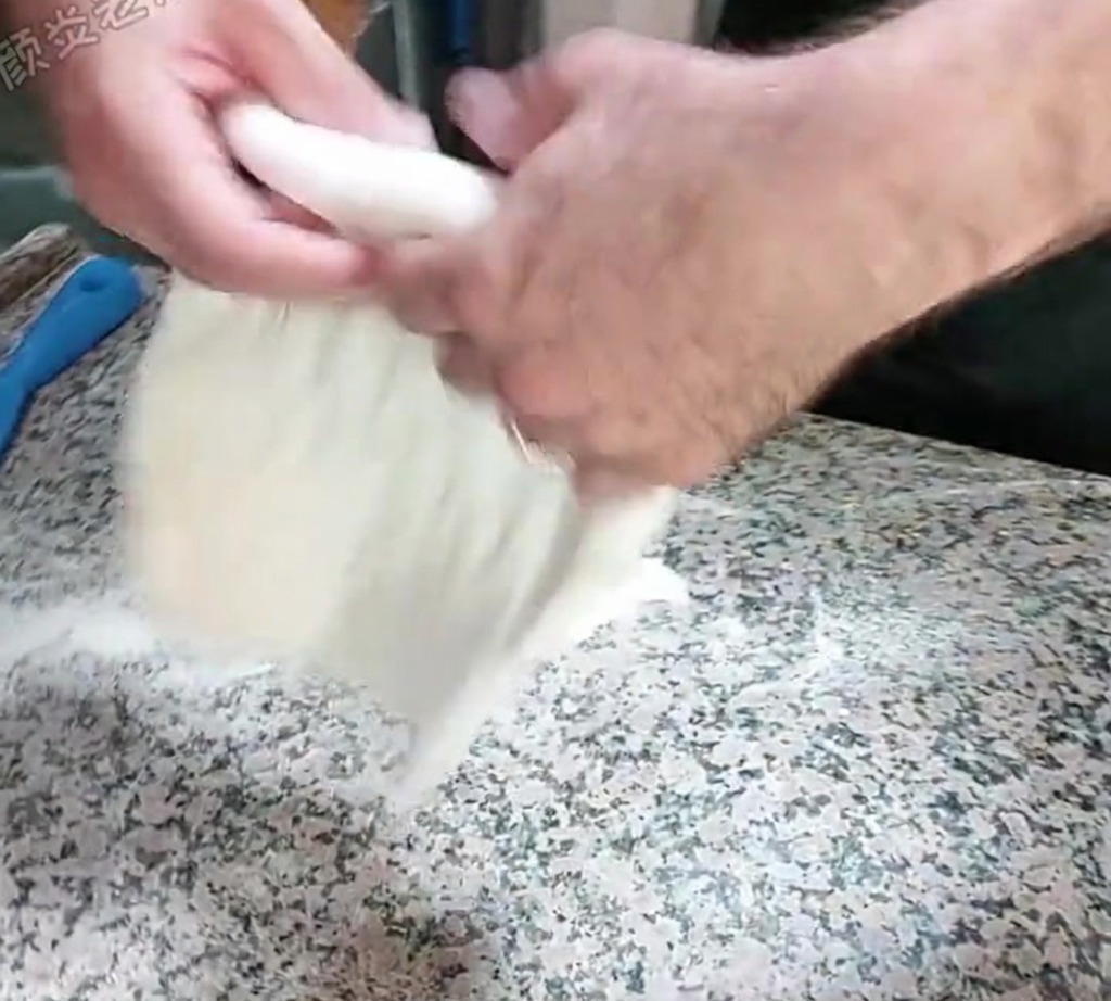 Masa siendo estirada a mano usando una técnica de palmoteo sobre una encimera enharinada.