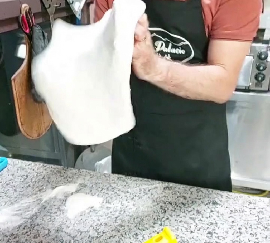 Una base de masa de pizza siendo moldeada lanzándola al aire.