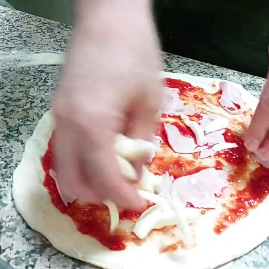 Trozos de queso mozzarella siendo añadidos a la base de la pizza.