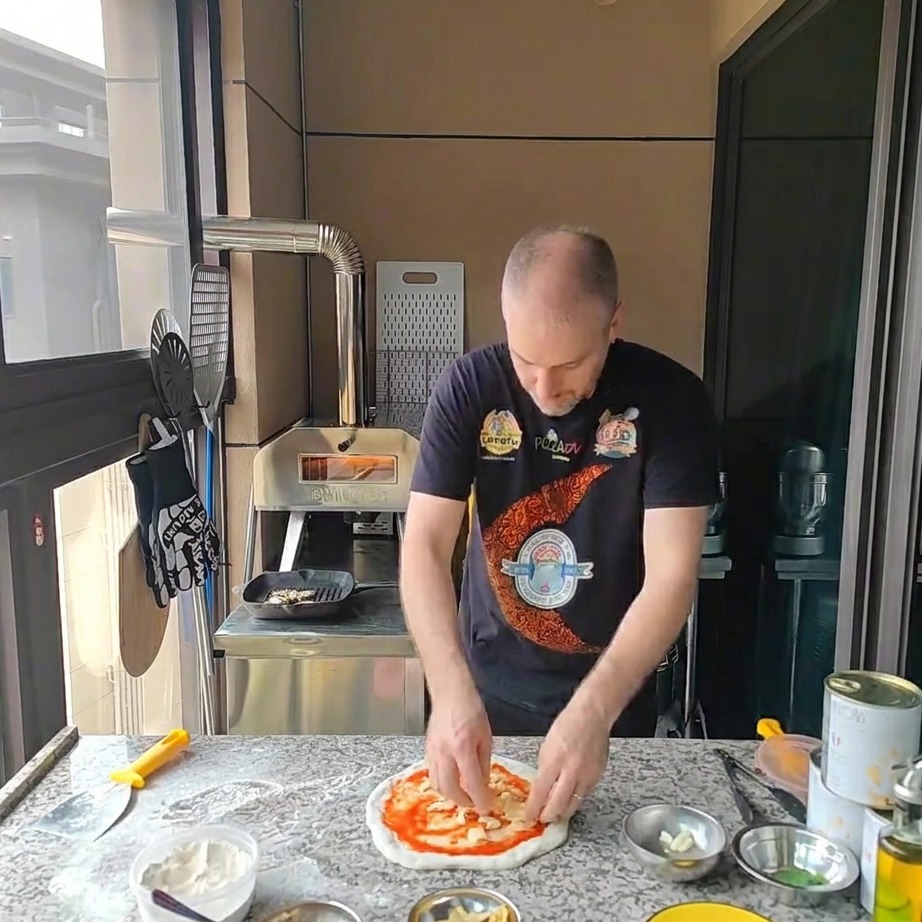 Queso mozzarella rallado siendo espolvoreado sobre la masa de pizza con salsa de tomate.