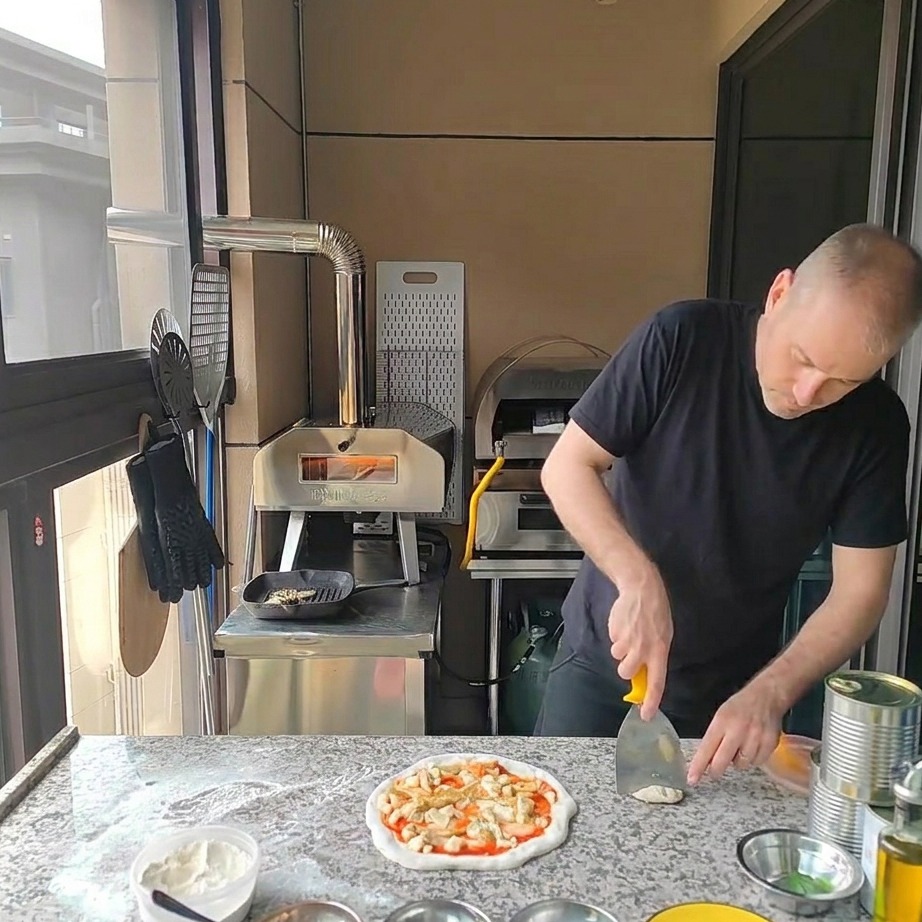 Trozos de pollo a la parrilla siendo colocados encima de la pizza con alcachofas y queso.