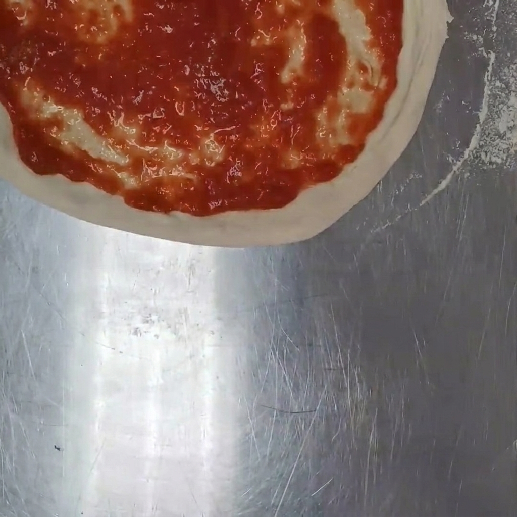 Trozos de queso mozzarella fresco siendo esparcidos a mano sobre la salsa de tomate en la masa de pizza.
