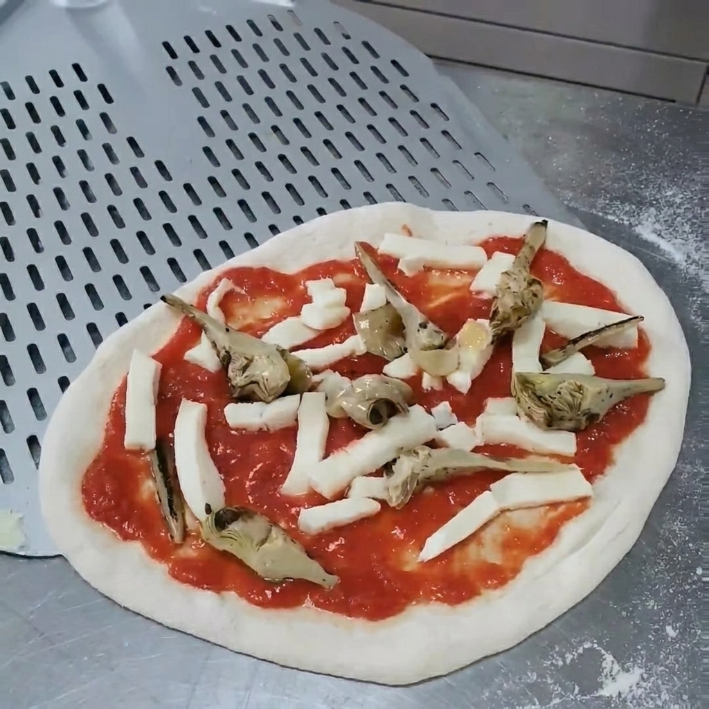 Manos ajustando la posición de las alcachofas a la parrilla sobre la pizza cruda para asegurar una cobertura uniforme.