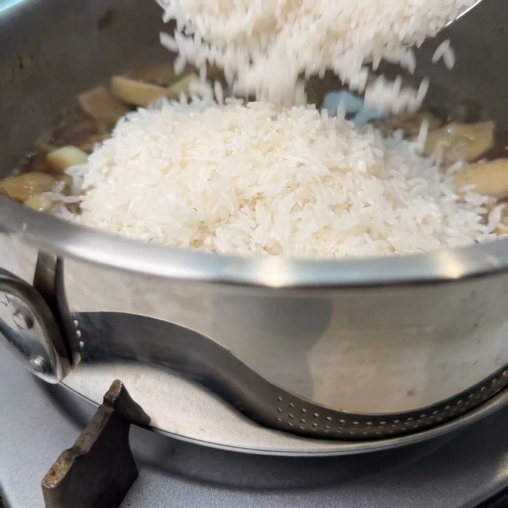 Arroz blanco previamente remojado siendo añadido a la olla con la mezcla de champiñones, seguido de agua.