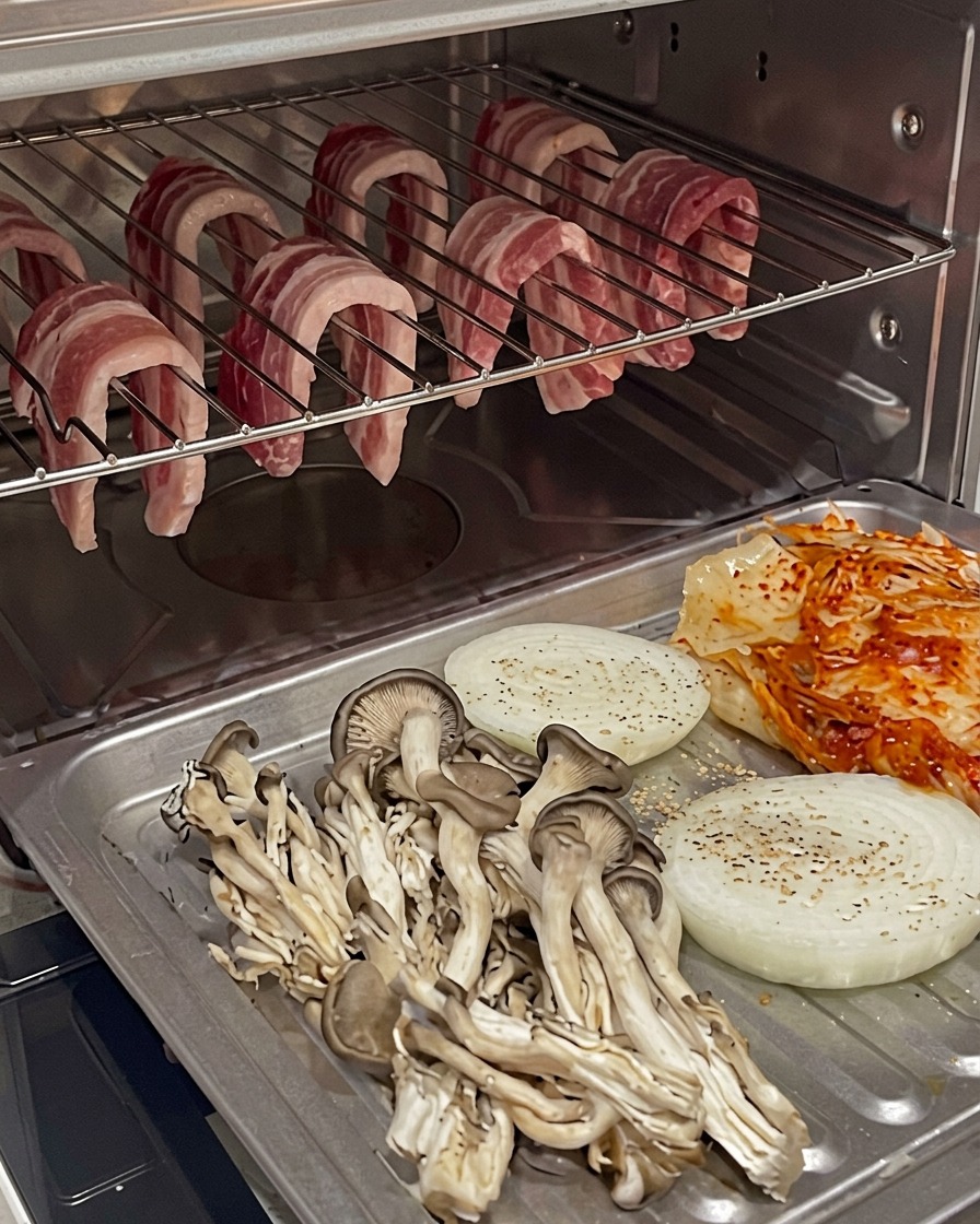 Bandeja de horno con verduras y kimchi posicionada debajo de la panceta colgada en el horno.