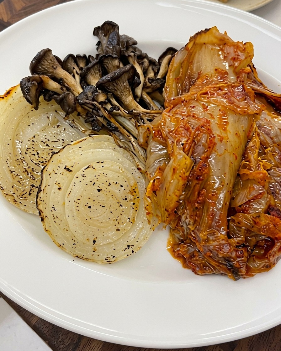 Semillas de sésamo siendo esparcidas sobre las verduras asadas y el kimchi en un plato.
