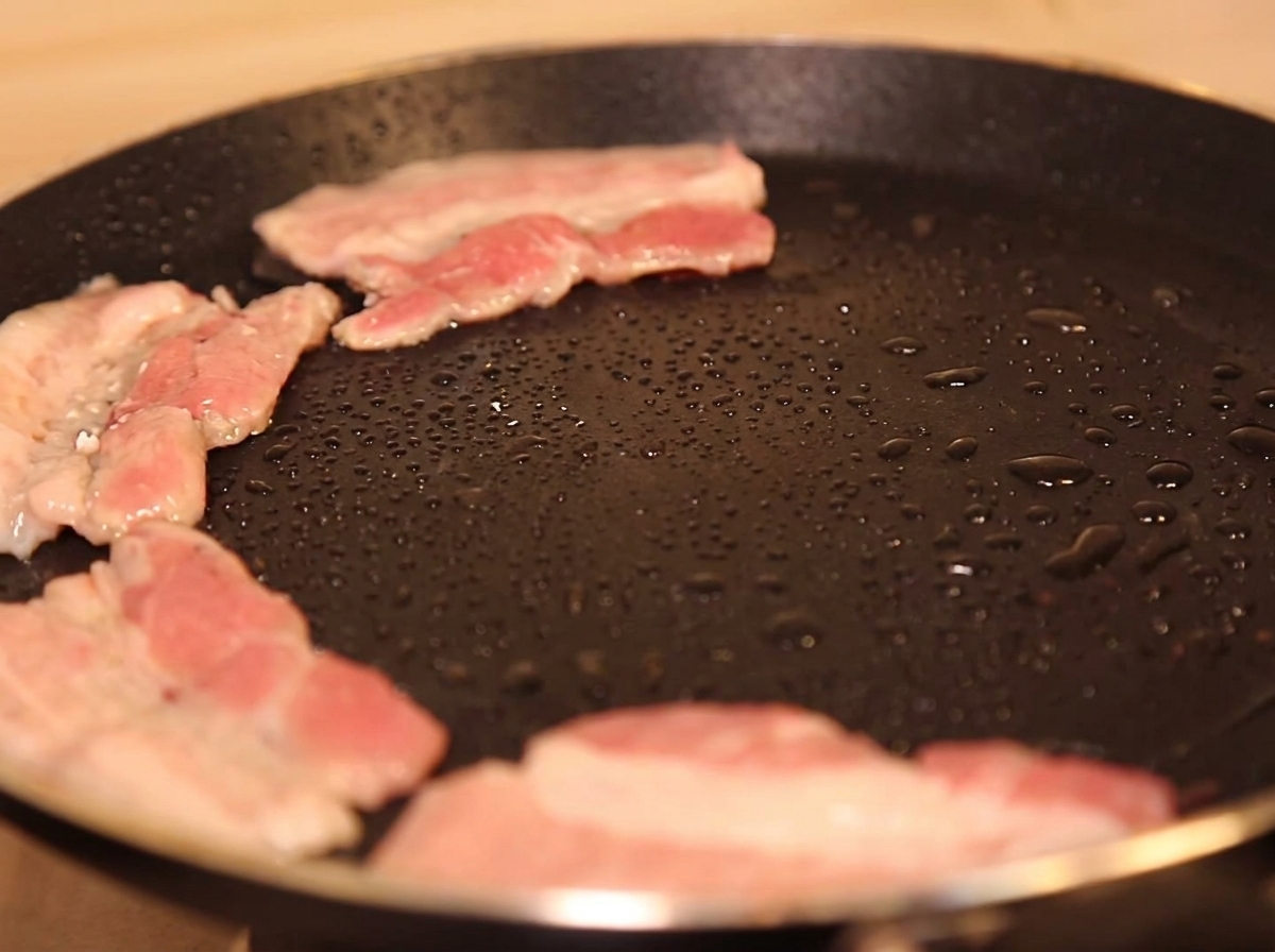 Rebanadas de panceta cocinándose en una sartén caliente con poco aceite, comenzando a dorarse.