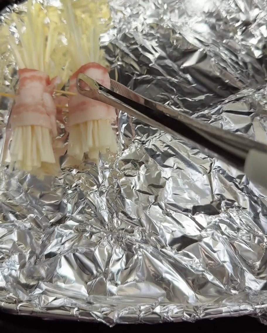 Rollitos de panceta y enoki colocados en la cesta de una freidora de aire forrada con papel de aluminio.