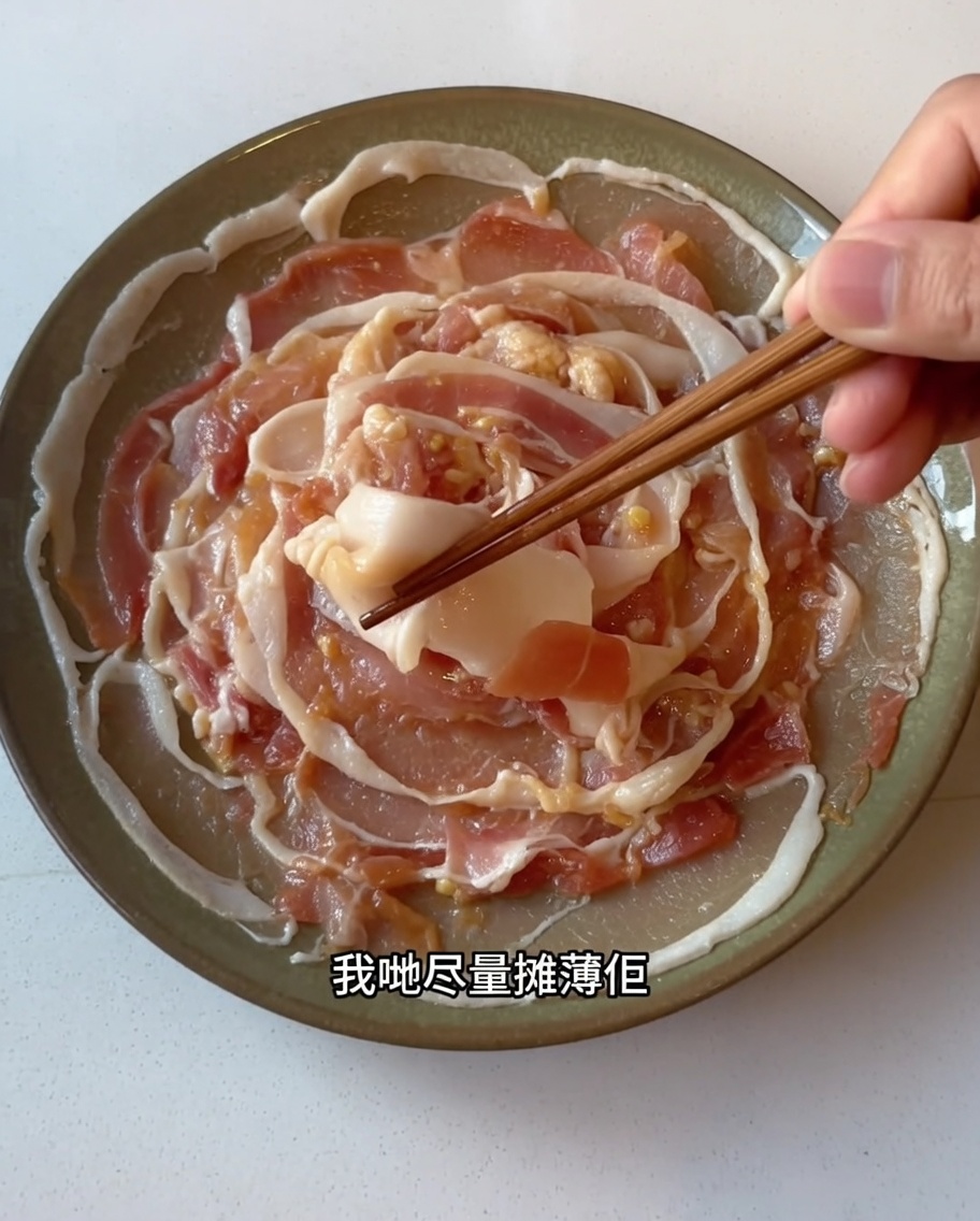 Rebanadas de panceta marinada siendo extendidas cuidadosamente en una sola capa sobre un plato utilizando palillos.