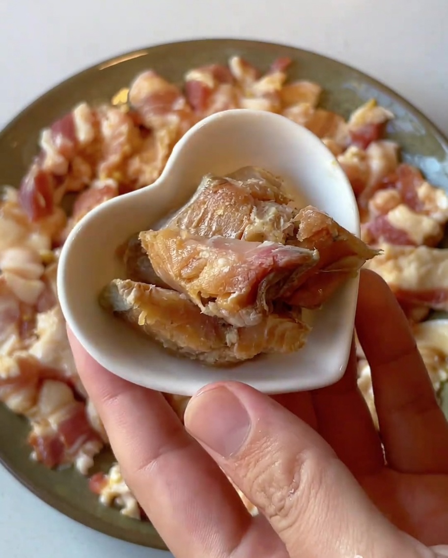 Primer plano de pequeños trozos de pescado salado en conserva colocándose sobre un plato de cerdo marinado crudo.
