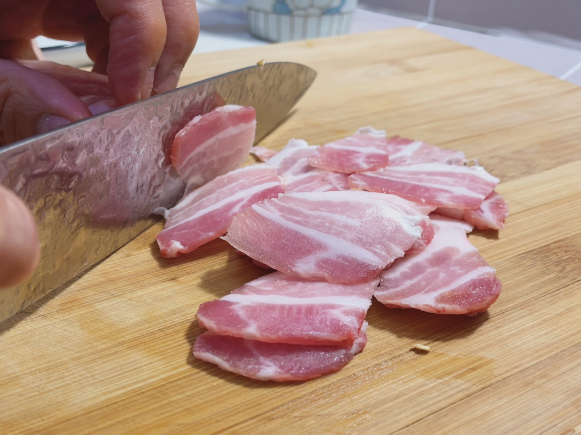 Tiras crudas de panceta dispuestas sobre una tabla de cortar de madera junto a un cuchillo de chef.