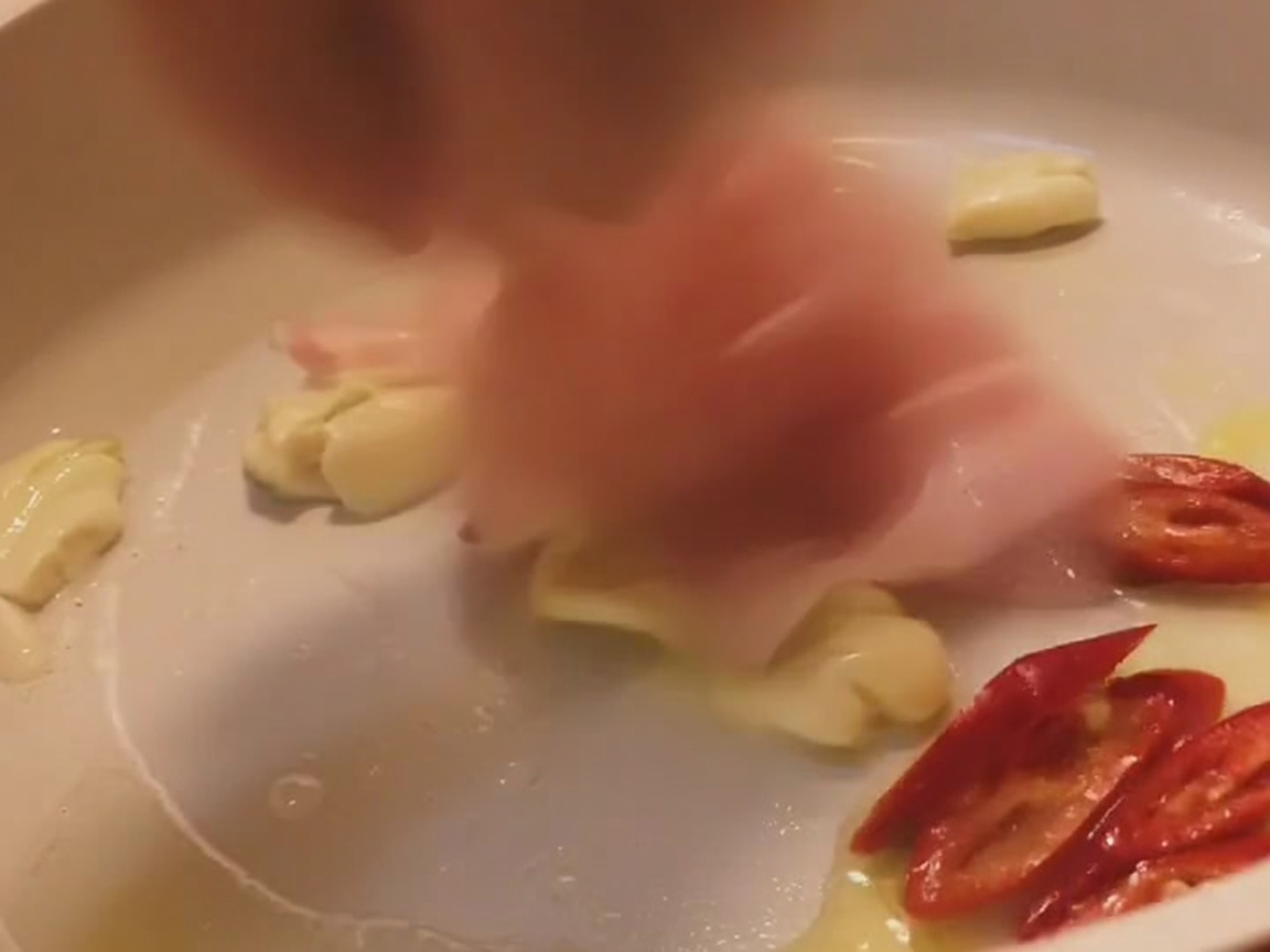 Tiras de panceta salteándose en una sartén de color claro con ajo y rodajas de chile rojo.