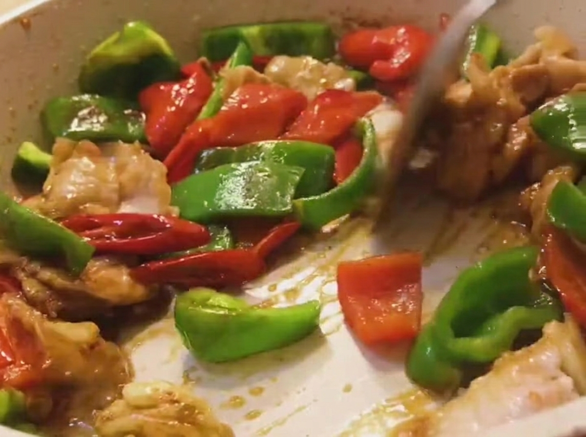 Una mezcla de carne, pimientos verdes y rojos siendo movida en una sartén con una espátula de madera.