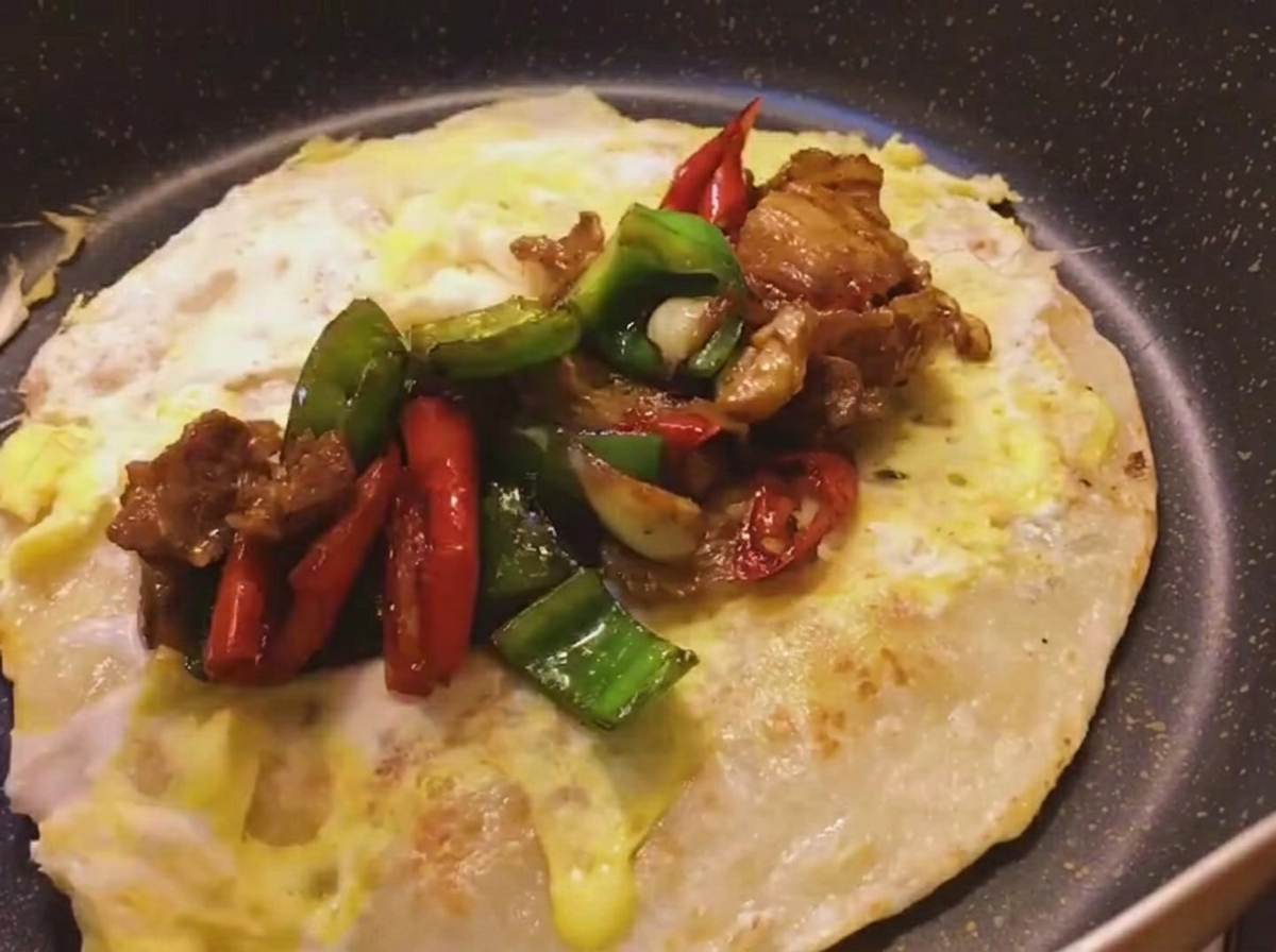 El relleno de panceta y pimientos siendo colocado sobre un pancake de cebolleta dorado con huevo.