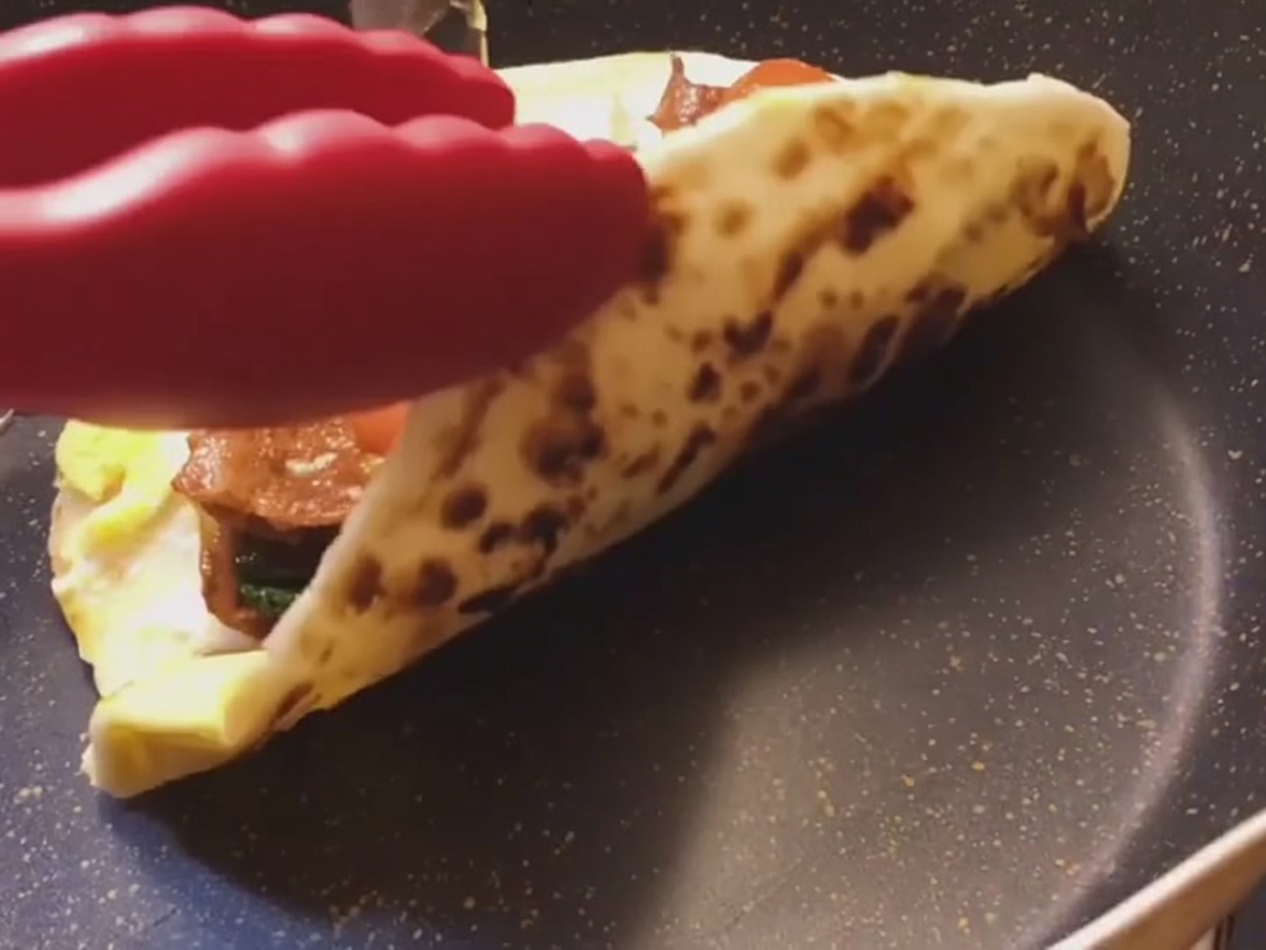 Un wrap de pancake de cebolleta siendo enrollado firmemente sobre una superficie plana.