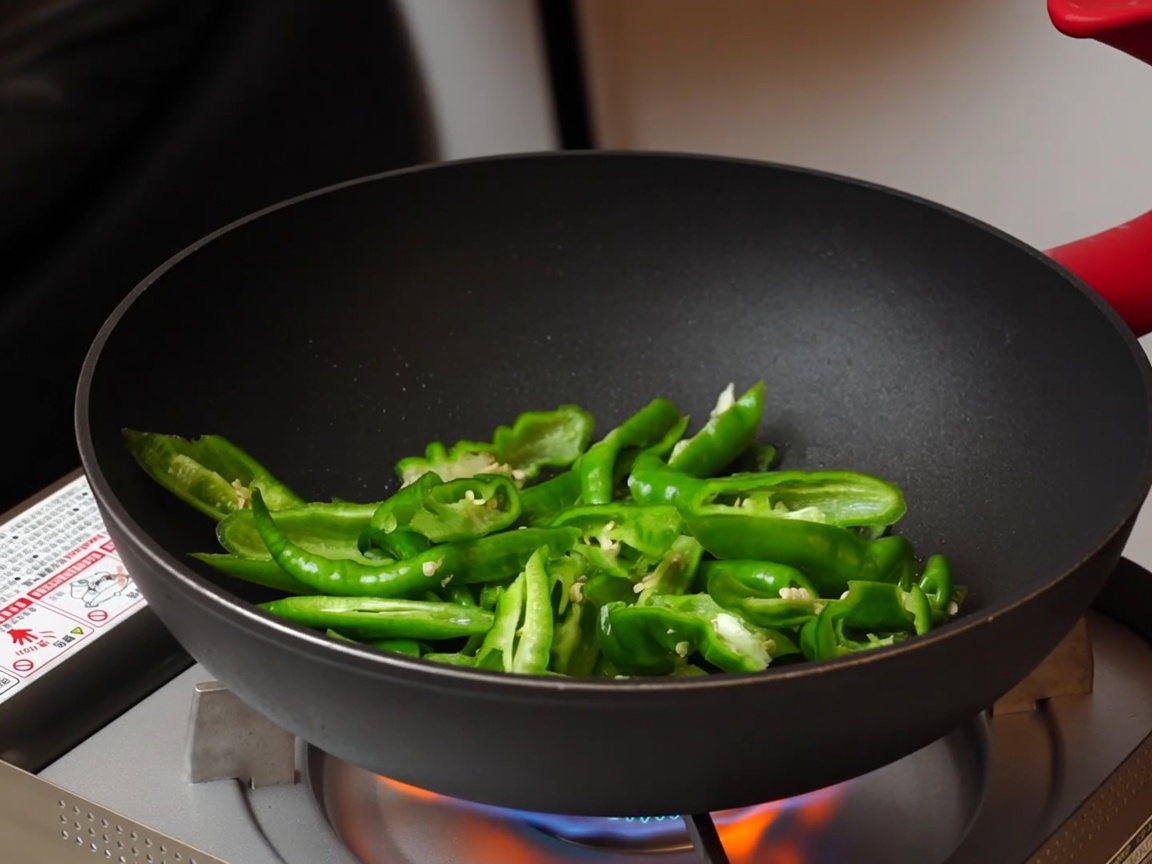 Pimientos verdes salteándose en una sartén antiadherente.
