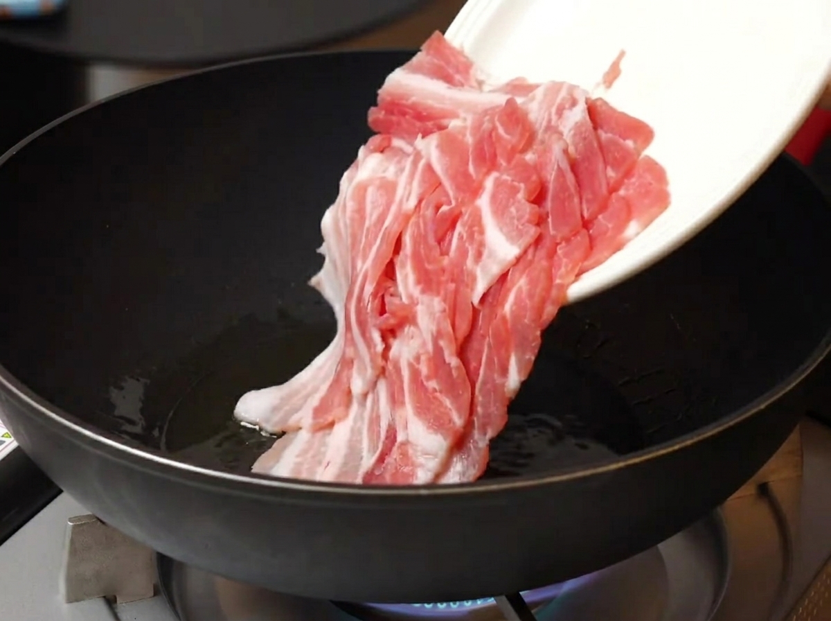 Panceta de cerdo cruda añadida a una sartén caliente con aceite.