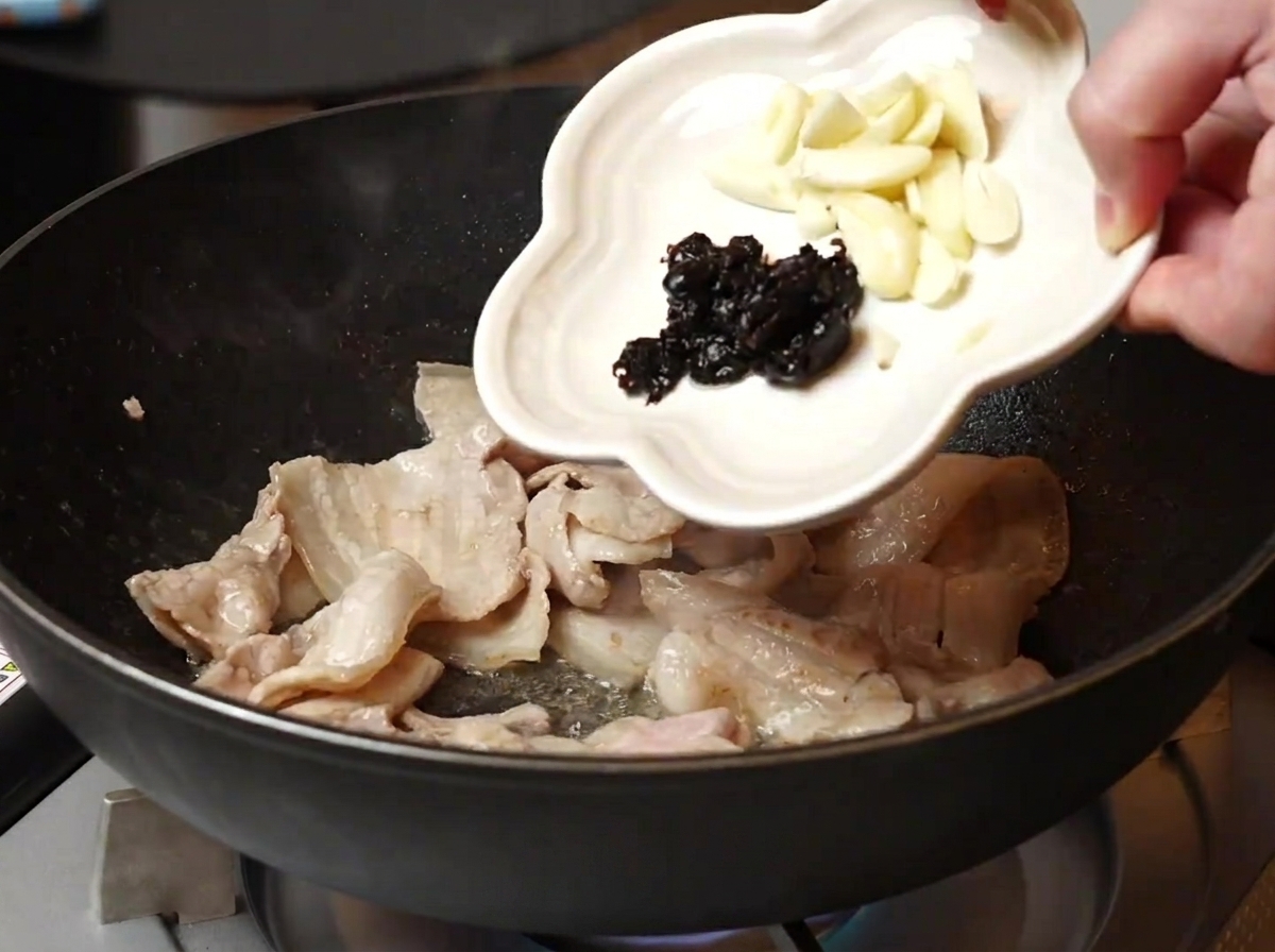 Ajo y frijoles negros añadidos a la sartén con la panceta cocinada.